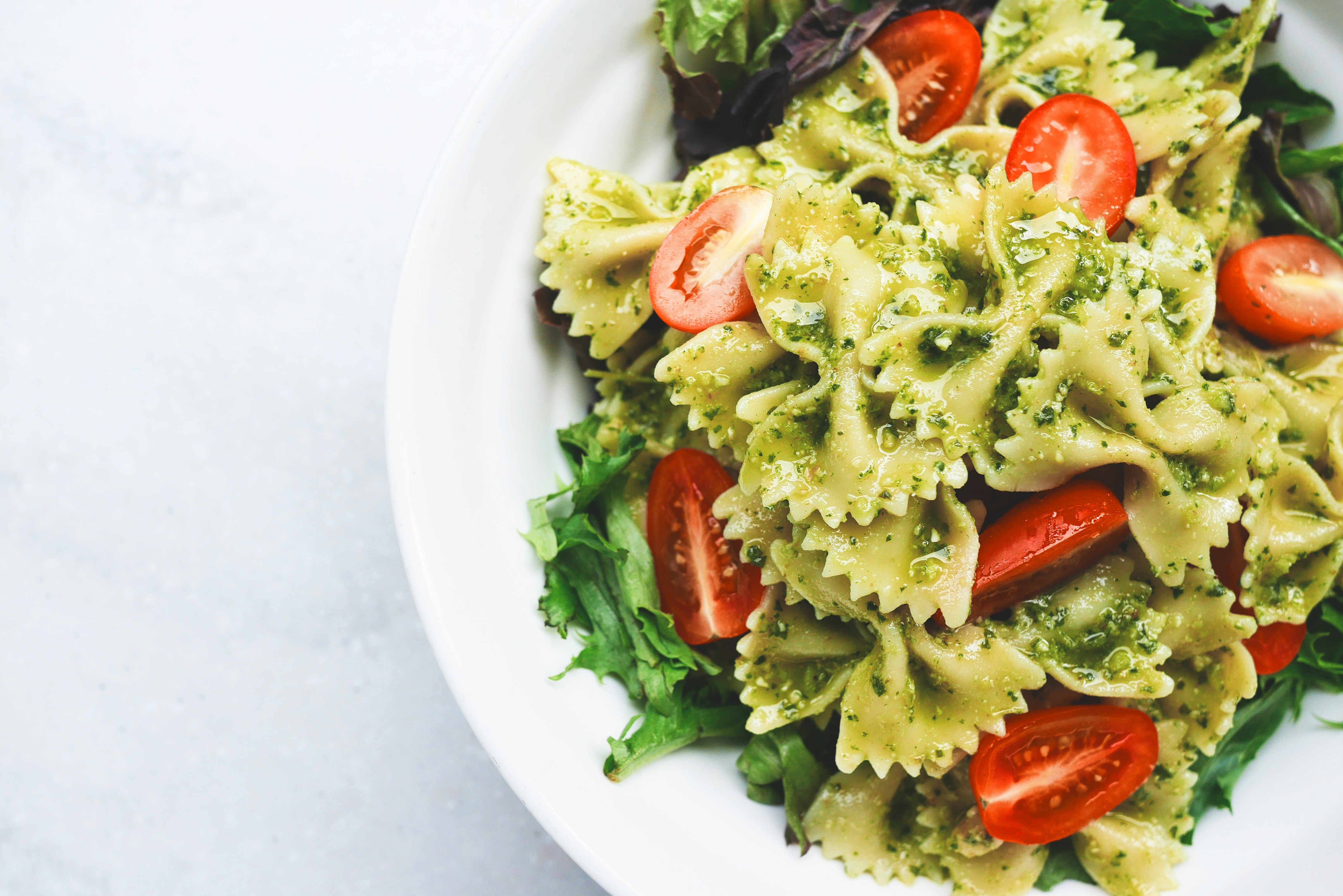 A plate of bow tie pasta, cherry tomatoes, lettuce, and pesto sauce 