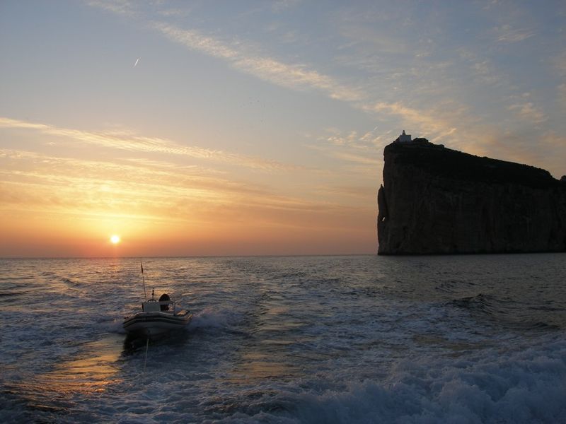 Small boat drives from Capo Cacci caves at sunset. 