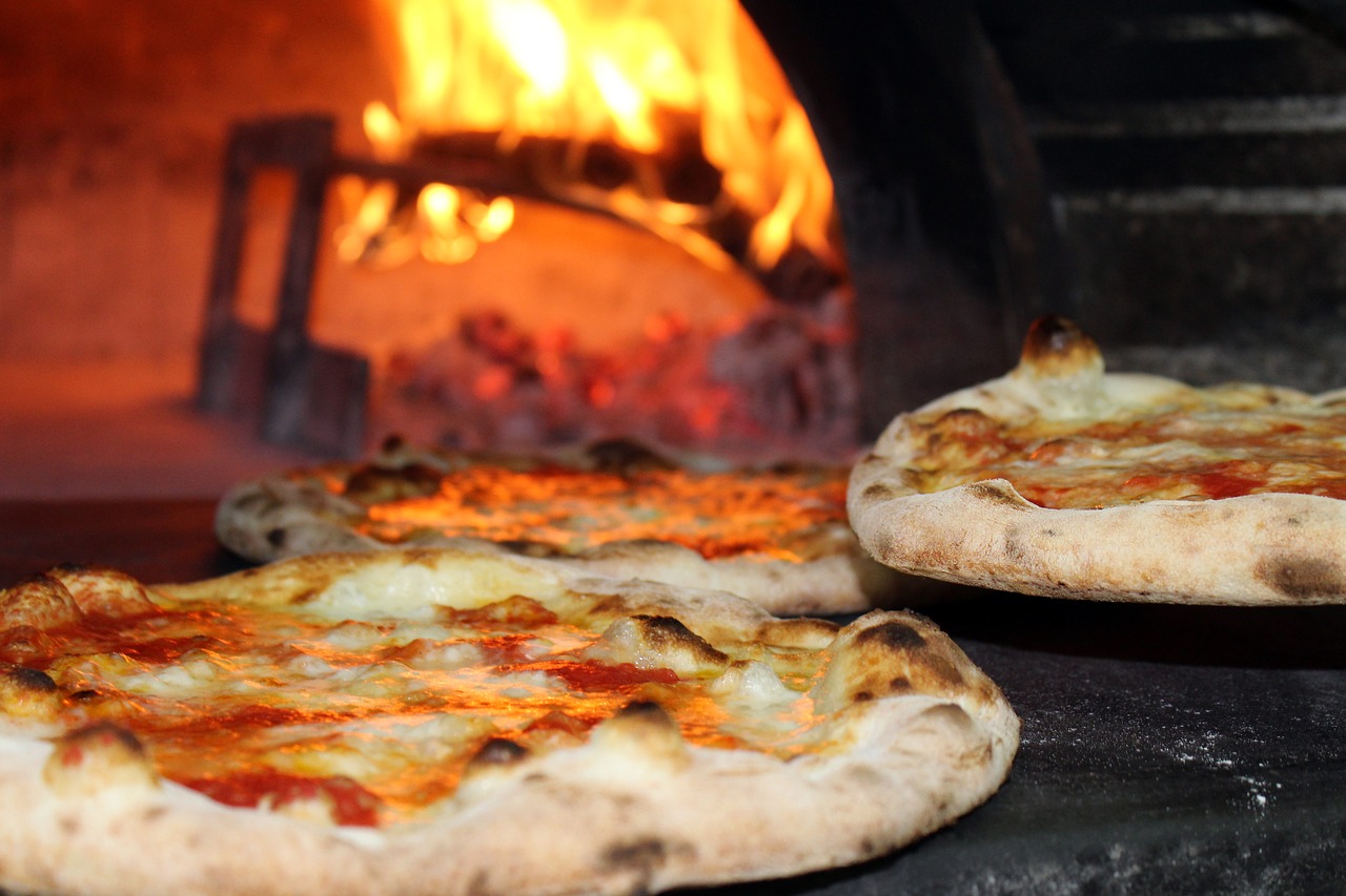 Two pizzas in front of a blazing pizza oven.