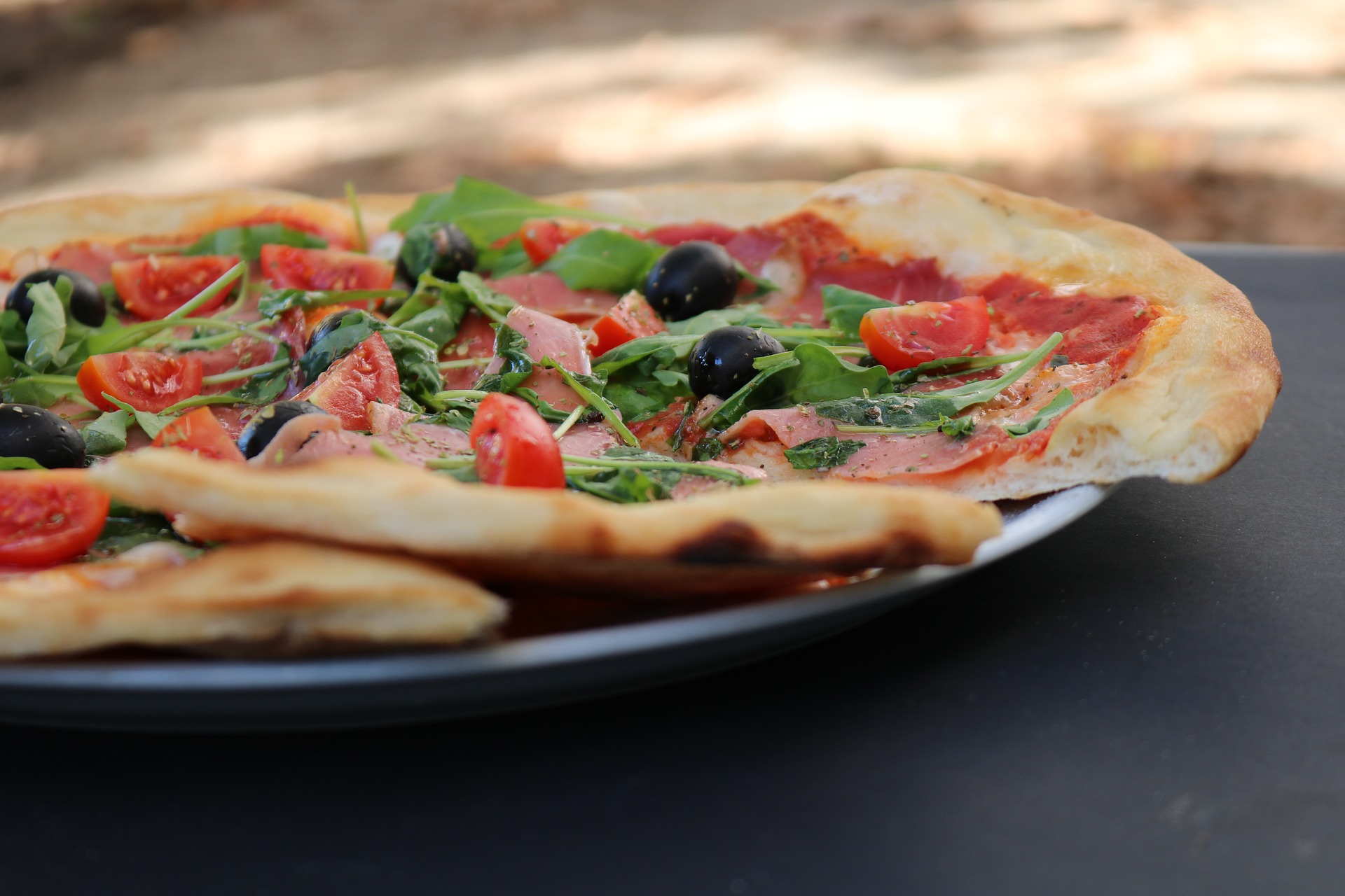 Fresh pizza on a plate with olive and ham toppings