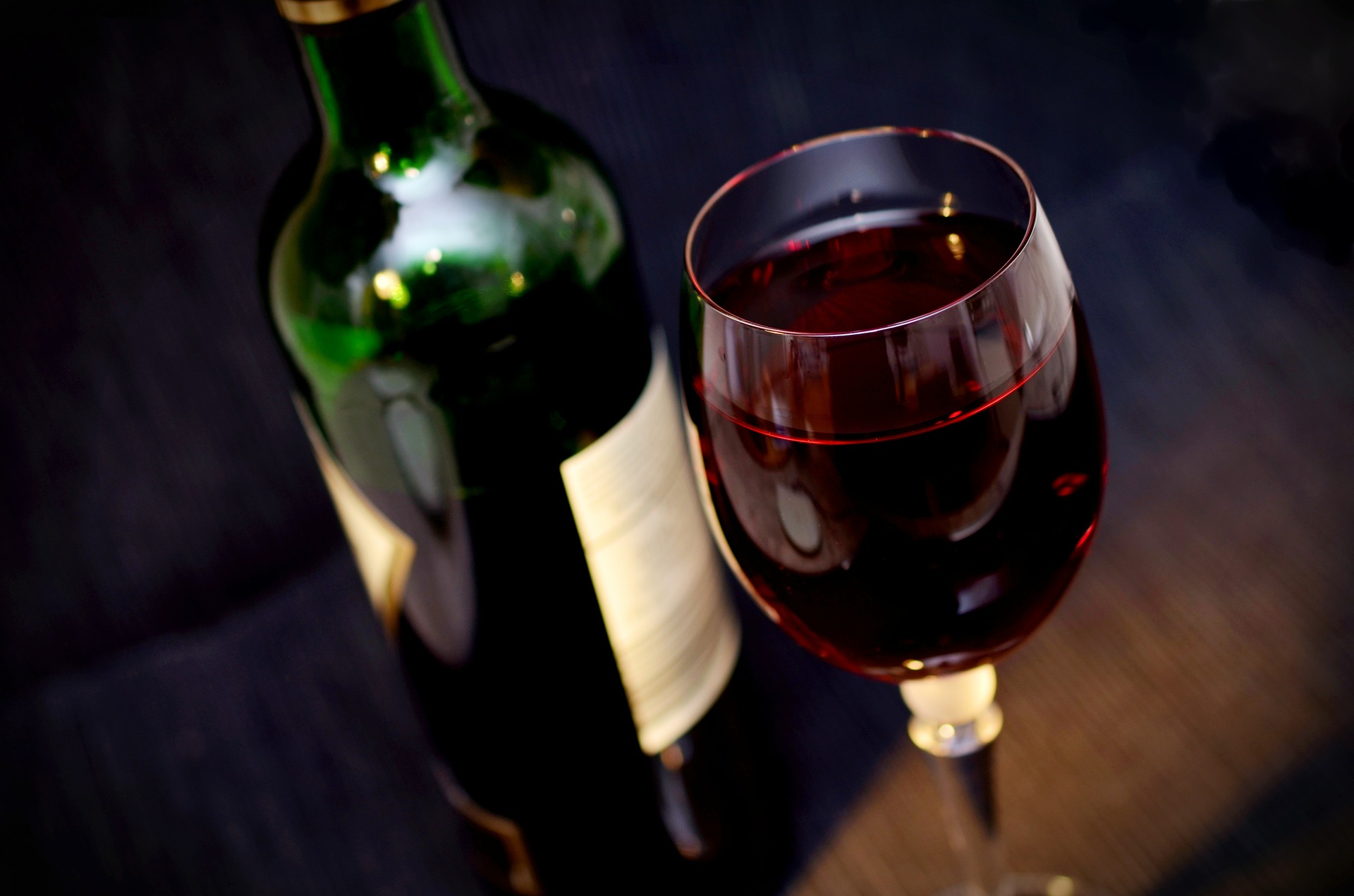 Glass of red wine in front of a bottle of red wine.